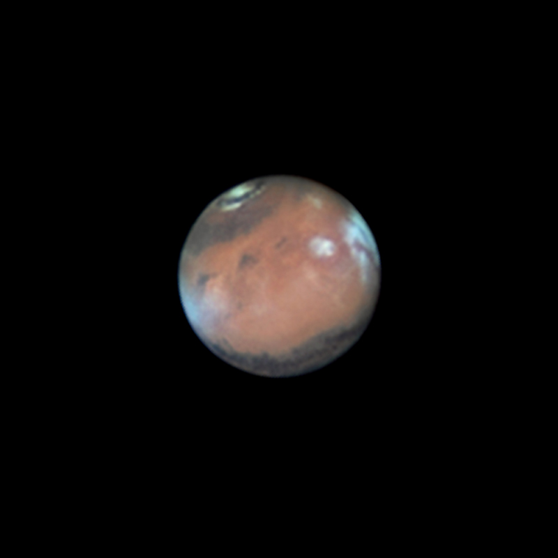 Mars ist sehr detailreich mitten im Bild vor einem schwarzen Hintergrund abgebildet. Oben ist eine Polkappe, rechts sind weiße Wolken.