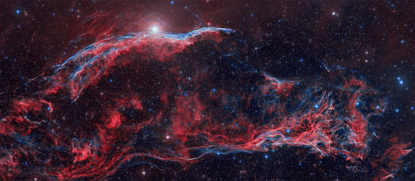 Im querformatigen Bild sind wild strukturierte Nebelfetzen verteilt. Sie leuchten blau und rot, was ihrer Zusammensetzung entspricht (Wasserstoff und Sauerstoff). Im Bild sind der Hexenbesen und Pickerings Dreieck zu sehen.