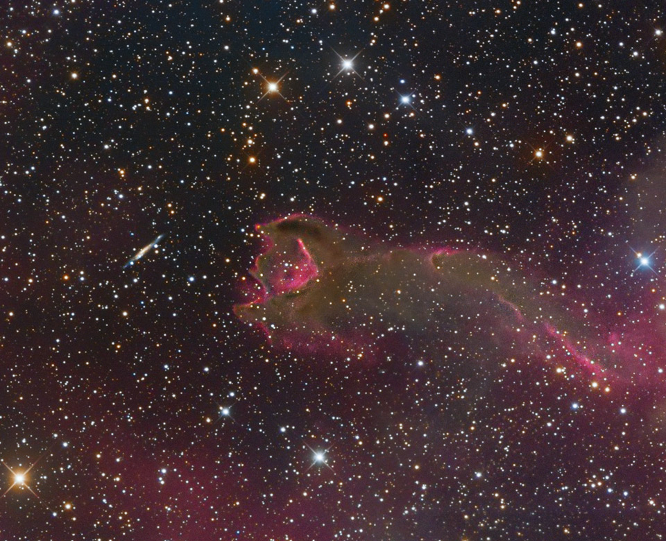 Das Bild ist dicht mit Sternen gesprenkelt. Es scheint, als würde eine wurmartige Kreatur nach einer Galaxie schnappen, die links im Bild schwebt.