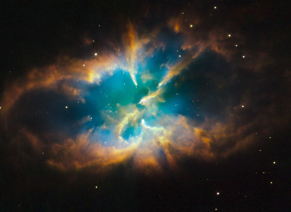 Zwischen sehr wenigen Sternen leuchtet der Nebel NGC 2818 im Sternbild Kompass (Pysis). Seine geschwungenen Ränder sind braunorange, das Innere leuchtet türkis-blau.