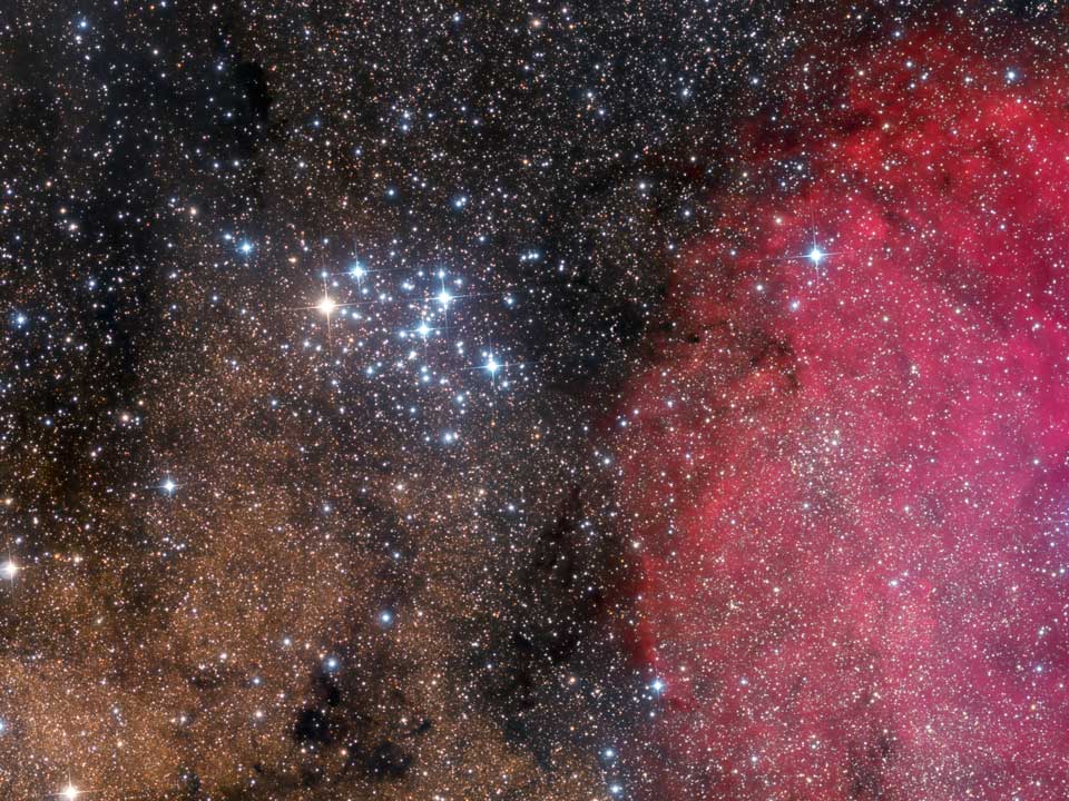 Mitten im Bild leuchtet der Sternhaufen M6 im Sternbild Skorpion. Sein Umriss erinnert an einen Schmetterling. Rechts leuchtet ein markanter roter Emissionsnebel. Der Hintergrund ist dicht von Sternen gesprenkelt.