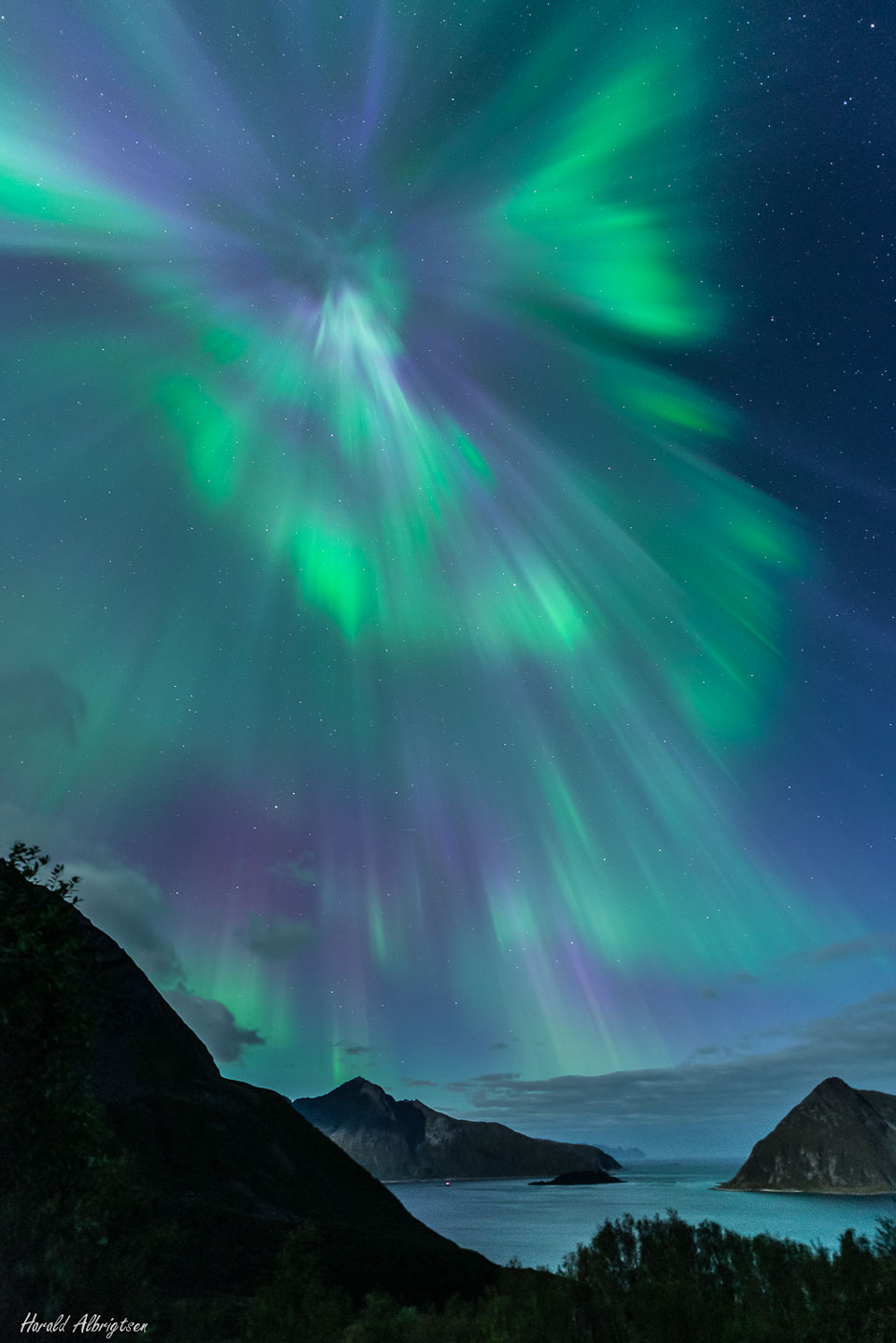 Über dem Sessøyfjorden und der norwegischen Insel Kvaløya breitet sich eine malerische Polarlichtkrone aus, die grün-violett schimmert.