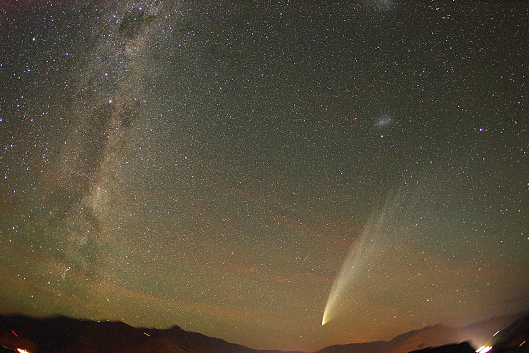 Über dem Mount Remarkable und Cecil Peak breitet Komet McNaught seinen fächerförmigen Schweif aus. Am sternklaren Himmel schimmert Nachthimmellicht. Links ist das Zentralband der Milchstraße, neben dem Kometen blitzt ein Meteor, darüber ist eine Sterneninsel.