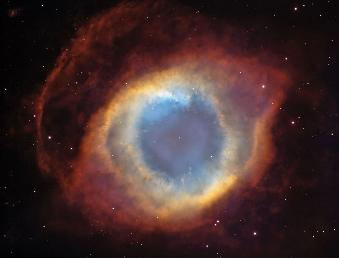 Der Helixnebel ist einer der prächtigsten planetarischen Nebel am Himmel. Er erinnert an ein riesiges Auge. Im Bild leuchtet das Innere wässrig blau, es ist von einem gelben gefaserten Ring umgeben, um den außen rote Nebelränder verlaufen.