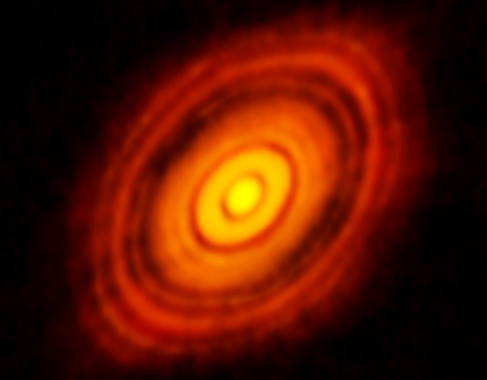 Die rot leuchtende Scheibe im Bild erinnert an den Querschnitt eines Baums mit Jahresringen.In der Mitte leuchtet die Scheibe gelb. Die dunklen Lücken stammen vielleicht von Planeten.