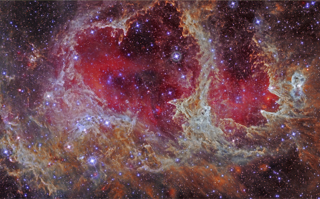 Die Region im Bild ist W5 oder der Seelenebel im Sternbild Cassiopeia. In der Mitte ist ein rot leuchtendes Herz, umgeben von beige-braunen Nebelfetzen. Sterne in der Höhle komprimierten wahrscheinlich das Gas im Nebel nach außen hin und lösten so neue Sternbildung aus. In den äußeren Nebelfetzen sind viele Säulen, in denen vielleicht gerade Sterne entstehen.