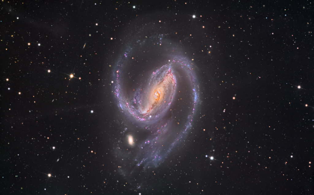 Die Spiralgalaxie mitten im Bild hat einen sehr ausgeprägten Balken, von dem zwei markante Spiralarme ausgehen. Links unten ist eine kleine Galaxie. Vier kaum sichtbare Sternströme entspringen dem Zentrum der Galaxie, sie bilden ein X.