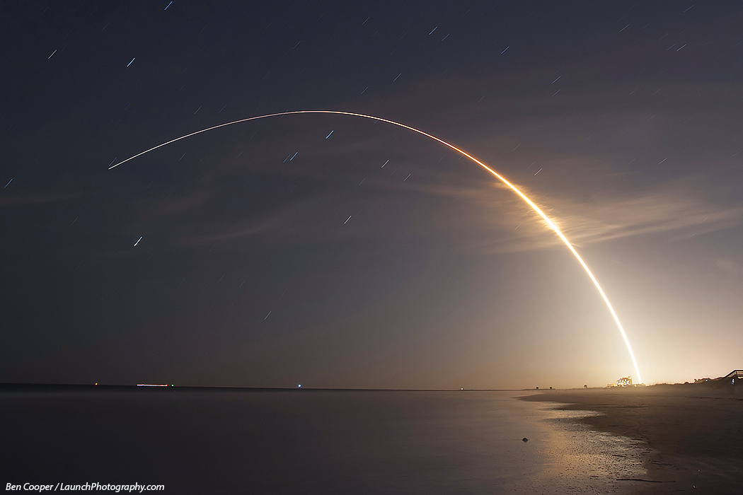 Hinter einer Bucht steigt der leuchtende Bogen eines Raketenstarts zum Himmel. Eine Atlas V brachte MMS in den Erdorbit.