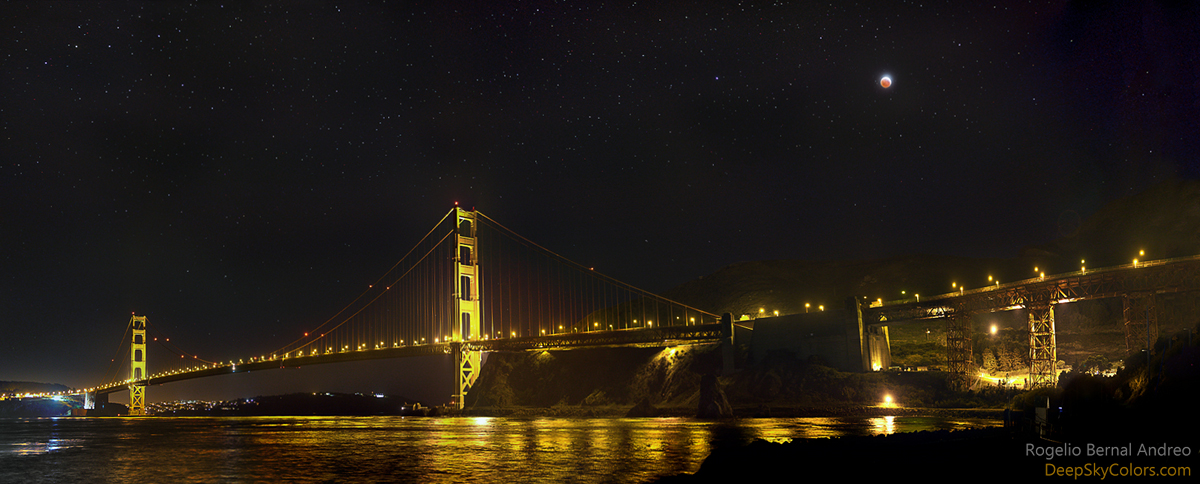 Über der Golden-Gate-Bridge leuchtet der total verfinsterte Mond. Brücke und Mond spiegeln sich im Wasser der San Francisco Bay Area.