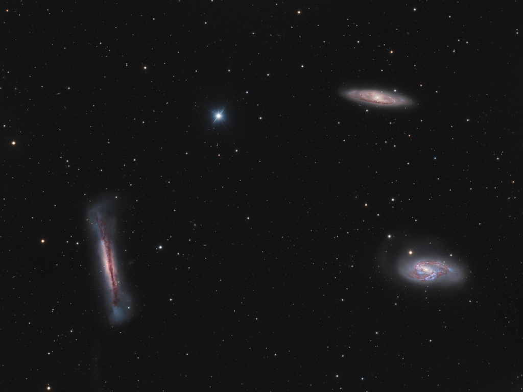 Die drei Galaxien im Bild sind Spiralgalaxien im Sternbild Löwe, die eng beisammen stehen. Die Galaxie links unten ist von der Kante zu sehen, ihre Scheibe wirkt fluffig. Durch die Mitte verläuft ein dunkles Staubband.