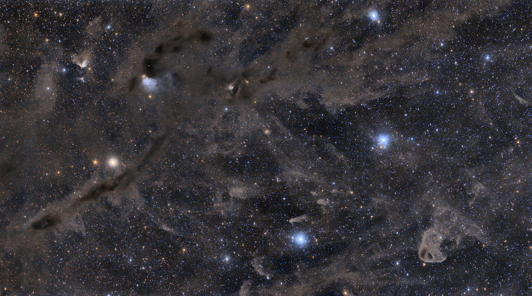 Dunkle Nebel durchziehen das Bild. Dazwischen leuchten einzelne blaue Reflexionsnebel um Sterne. Links oben ist der Nebel VdB 27 beim veränderlichen Stern RY Tau, rechts unten der kleine Adlerkükennebel, er steht Kopf.