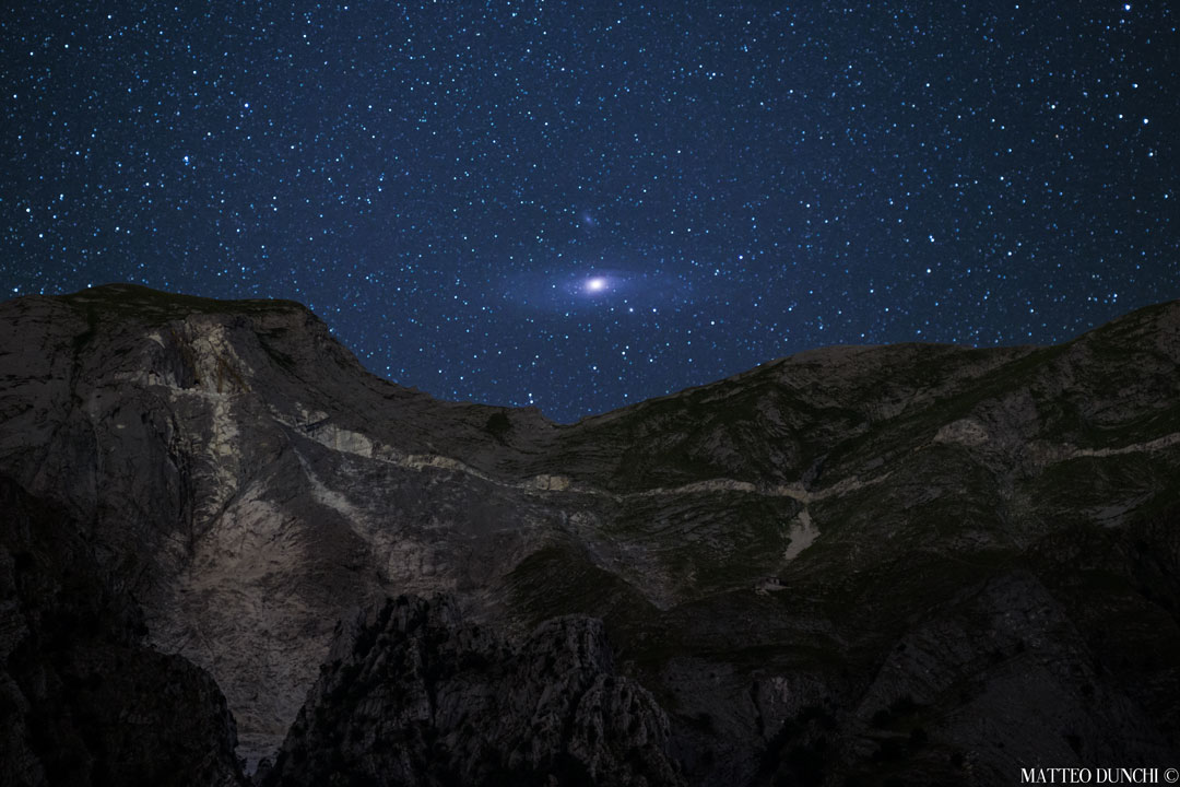 Über einem bergigen Horizont in den italienischen Alpen geht die Andromedagalaxie M31 auf.