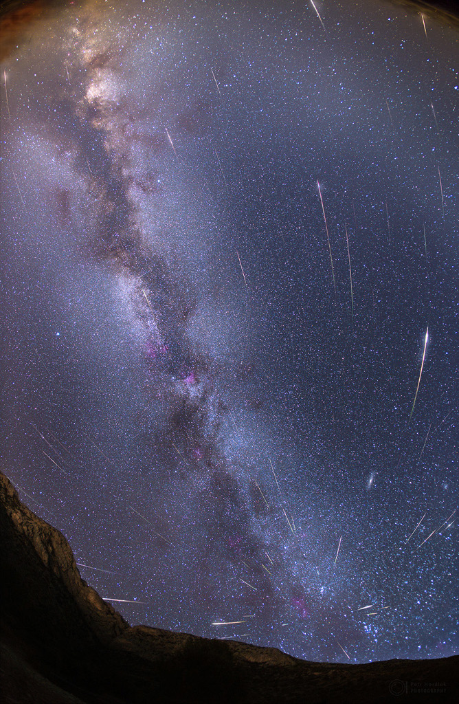 Über dem dunklen Horizont strömen viele Meteore von einem Punkt im Sternbild Perseus aus, es ist der Radiant der Perseïden. Hinten sind Zodiakallicht und die Milchstraße.