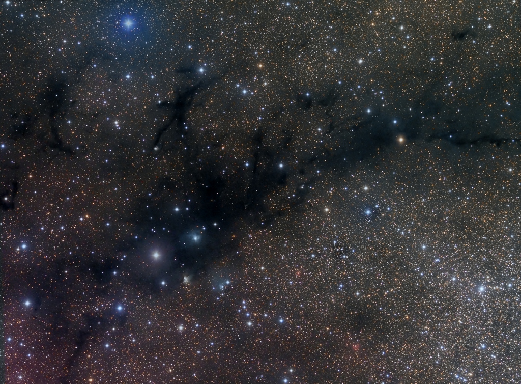 Vor einem dicht mit Sternen gespickten Hintergrund verlaufen dunkle Wolken, die an Strichmännchen erinnern, davor leuchten einige hellere Sterne.