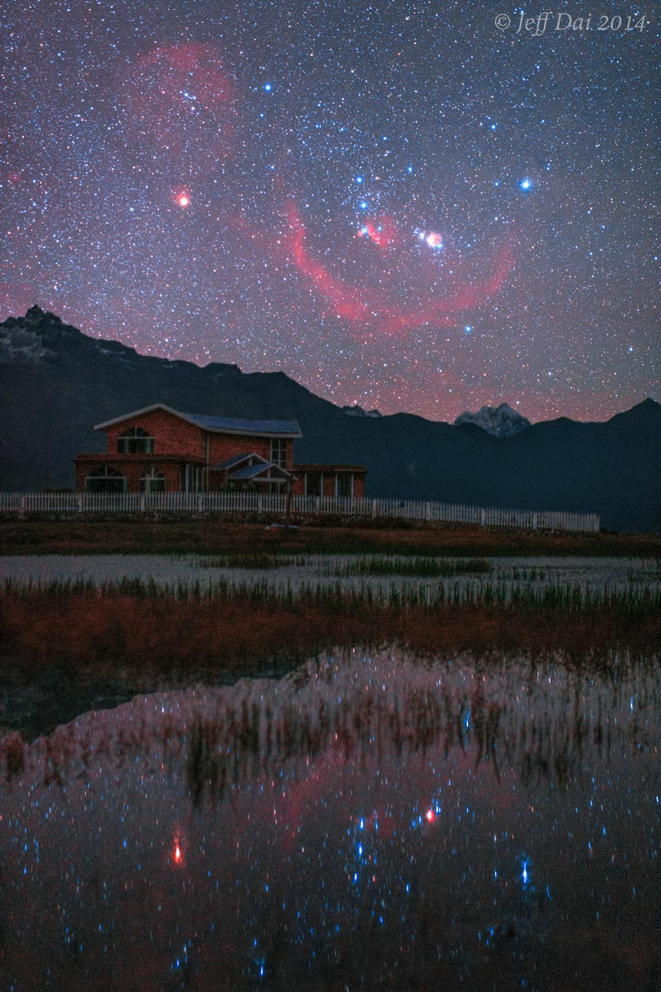 Über dem Himalaja geht das Sternbild Orion auf, zusammen mit der Barnardschleife, Rigel und Beteigeuze. Der Himmel spiegelt sich in einem ruhigen See im Vordergrund.