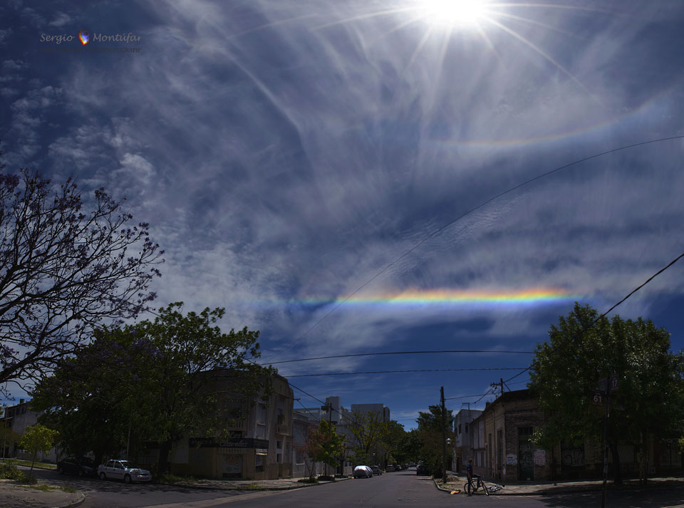Am heiteren Himmel über Buenos Aires leuchtet ein seltener Zirkumhorizontalbogen. Eiskristalle in Federwolken zerlegen Sonnenlicht in seine Spektralfarben.