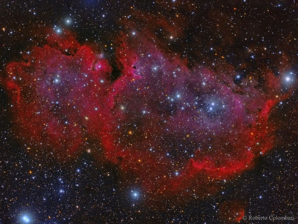 Hinter Sternen leuchten zwei dunkelrote, schwach leuchtende runde Nebelwolken.