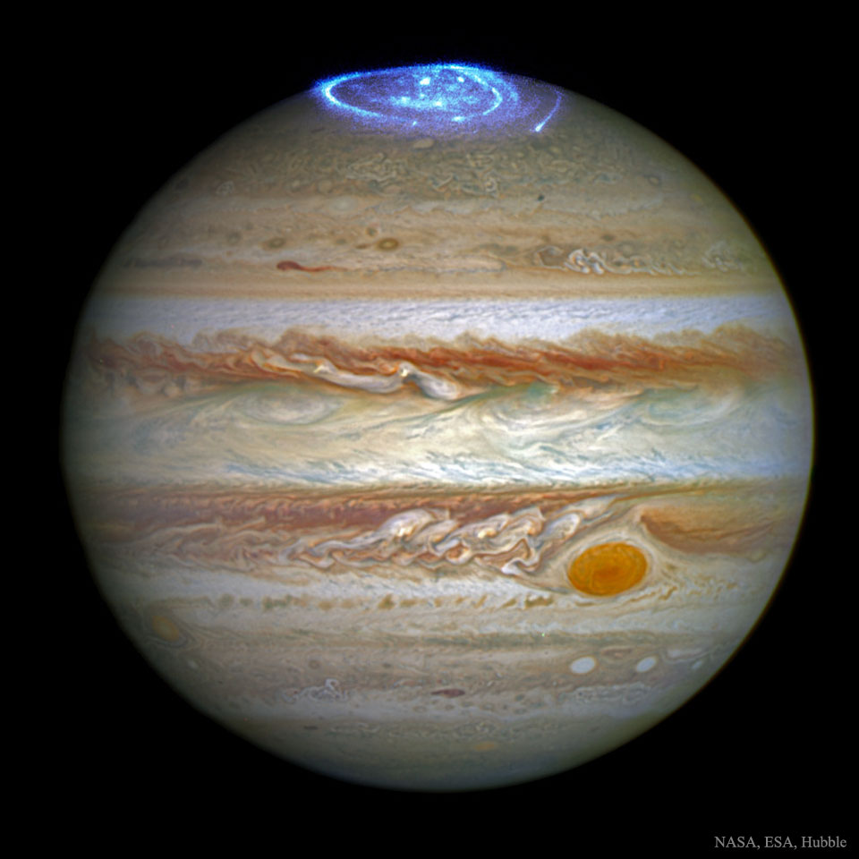 Bildfüllend ist der Planet Jupiter dargestellt. Die lebhaften Wolkenbänder sind detailreich abgebildet, rechts unten ist der große Rote Fleck. Oben leuchtet ein blaues Polarlicht.