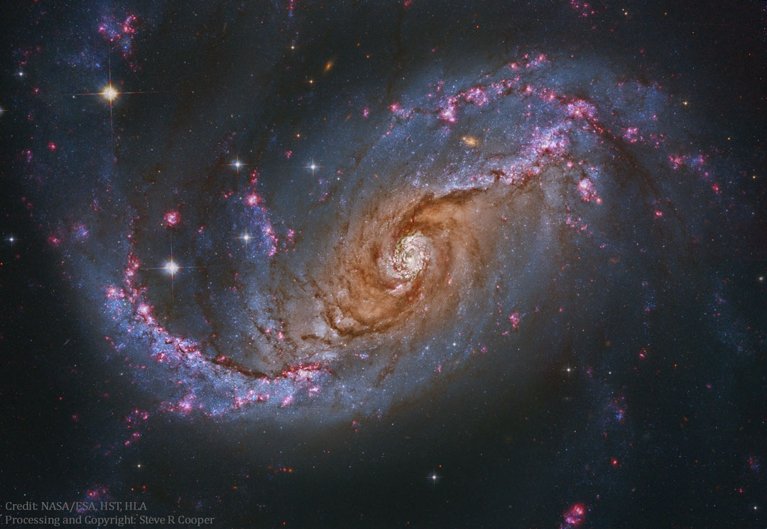 Diagonal füllt eine ovale Spiralgalaxie das Bild. Sie ist von mächtigen Staubwolken überzogen. Innen leuchtet sie dunkelorange, außen befinden sich viele blaue Sternhaufen und rote Sternbildungsgebiete in den Spiralarmen.