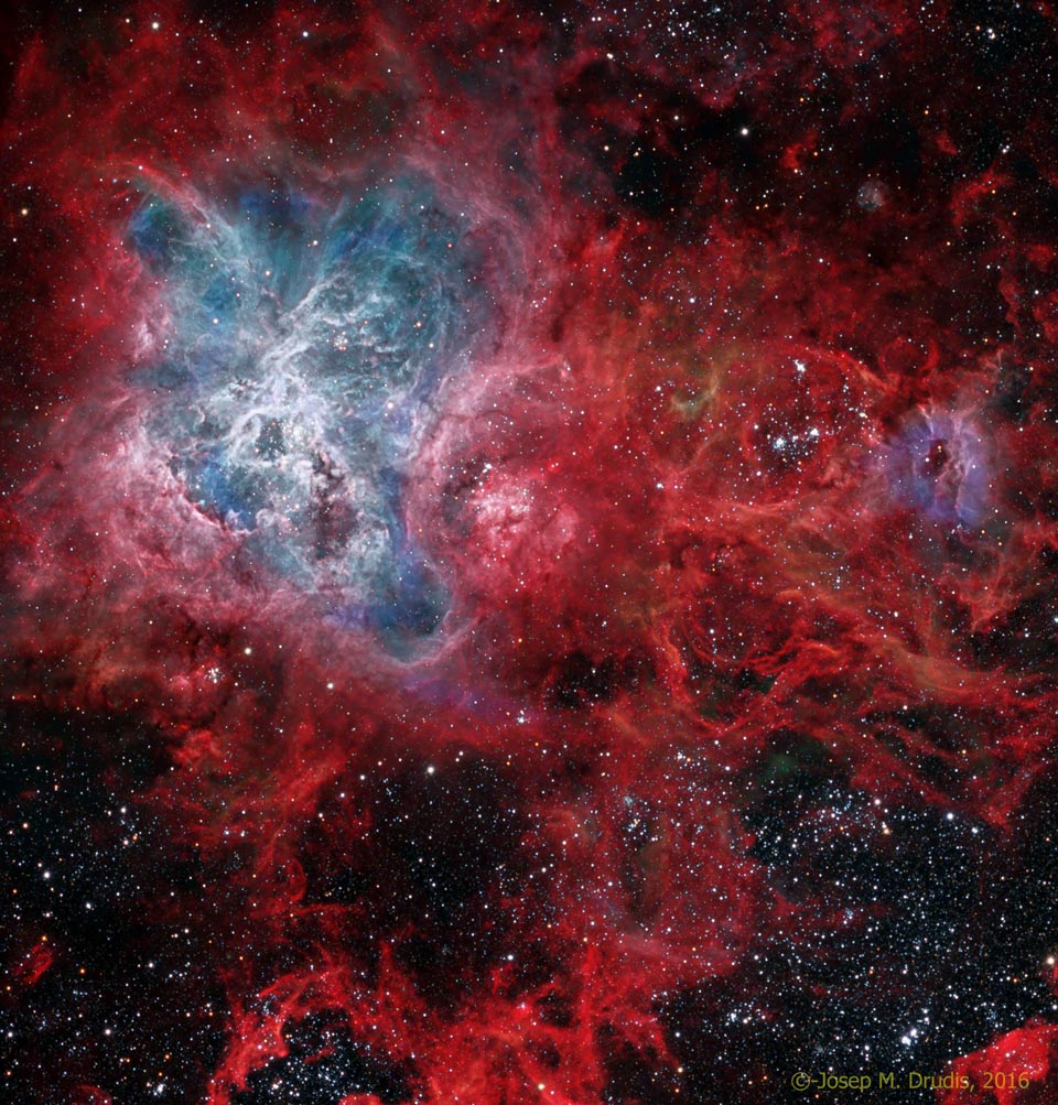 Der Tarantelnebel leuchtet links oben in blauen Tönen, er ist von roten Nebelwolken umgeben. Das Bild ist auch von vielen Sternen bedeckt.