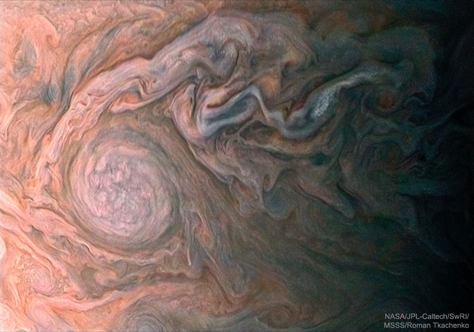 Links ist ein ovales Sturmsystem auf Jupiter, das von stark verwirbelten Wolken umgeben ist. Rechts beginnt der Terminator, die Schattenlinie auf dem Planeten.