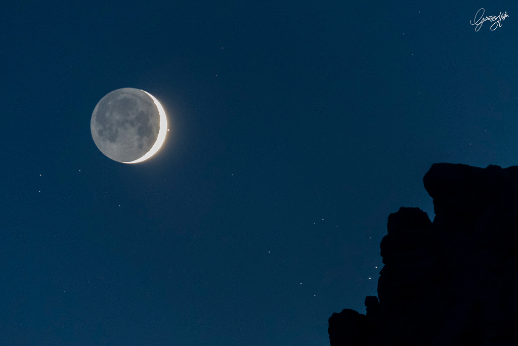 Hinter den Dolomiten leuchten helle Sterne. Neben dem Sichelmond strahlt der helle Stern Aldebaran. Die dunkle Seite wird von der Erde schwach beleuchtet.