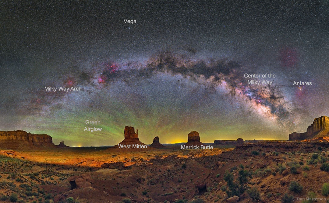 Über dem Monument Valley wölbt sich die Milchstraße mit dichten Staubwolken über den berühmten Tafelbergen. Hinter den Tafelbergen leuchtet Nachthimmellicht.