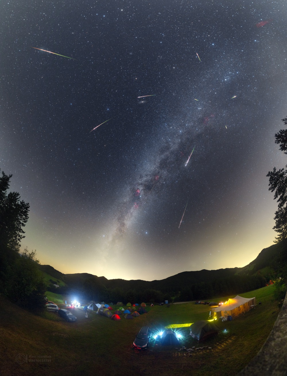 Über einem Lager von Sternfreunden steigt die Milchstraße nach rechts auf. Am Himmel zischen Meteore der Perseïden über den Himmel. Sie strömen vom Sternbild Perseus aus.