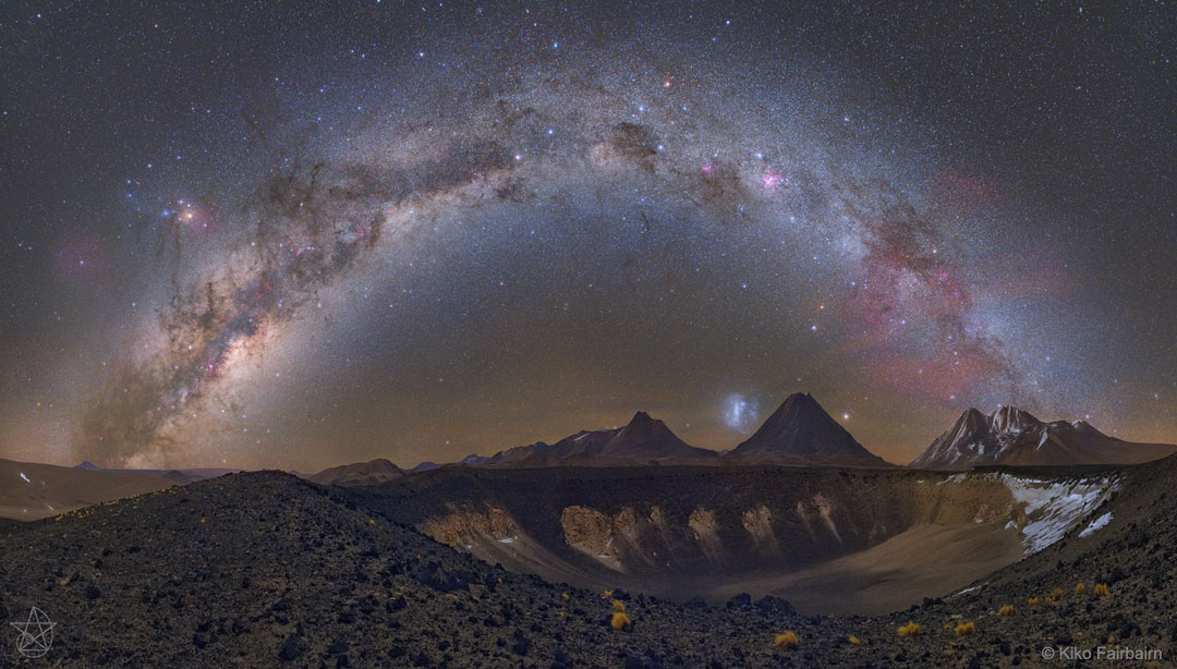 Über dem Rand einer Caldera wölbt sich die Milchstraße. Am Himmel leuchten Antares, der Gum-Nebel, die Große Magellansche Wolke und das Sternbild Kreuz des Südens.