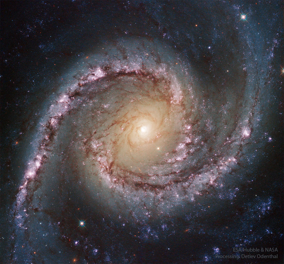 Bildfüllend ist eine von oben sichtbare Grand-Design-Spiralgalaxie mit zwei ausladenden Armen abgebildet. Das Zentrum leuchtet hellgelb, die Spiralarme sind von rosaroten Sternbildungsregionen markiert, in der ganzen Galaxie sind Staubnebel verteilt.