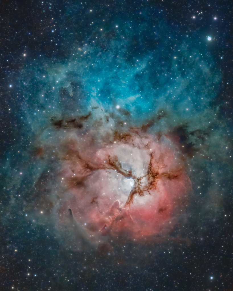 Mitten im Bild leuchtet eine rote Nebelwolke mit einem hellen Inneren, über dem ein Dreizack aus dunklen Wolkenranken liegt. Darüber ist ein blau leuchtender Reflexionsnebel.