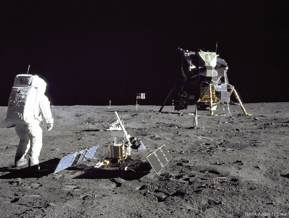 Der Apollo 11-Astronauten Buzz Aldrin steht neben dem gerade aufgestellten Mondseismometer. Er schaut zur Landefähre, dem Lunar Landing Module.
