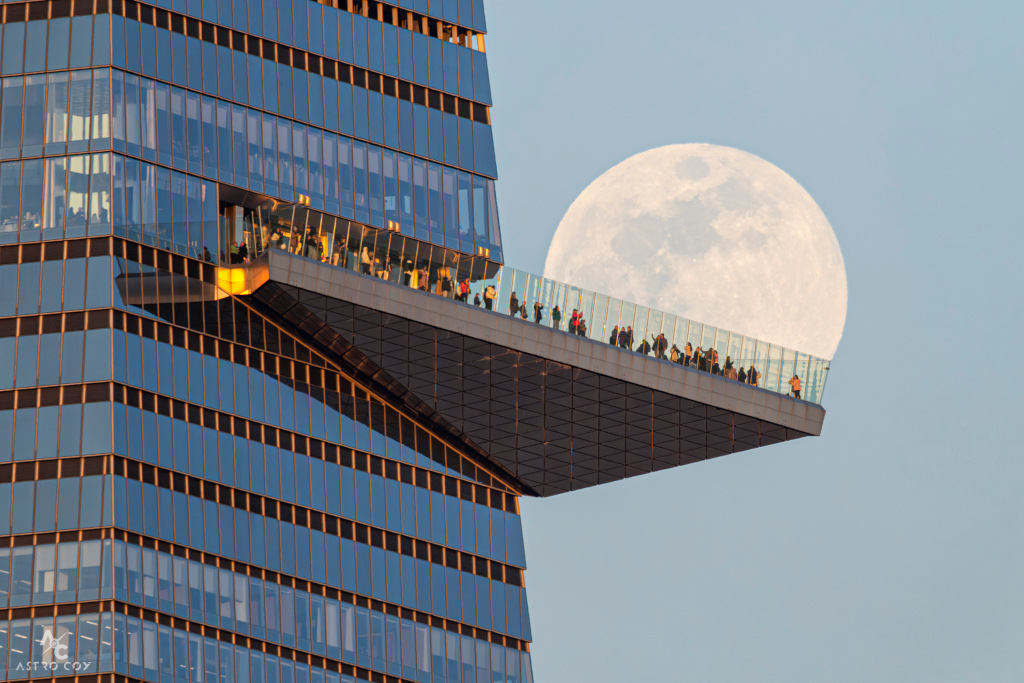 Über einer Plattform, die aus einem Hochhaus ragt, hängt der voll beleuchtete Mond.