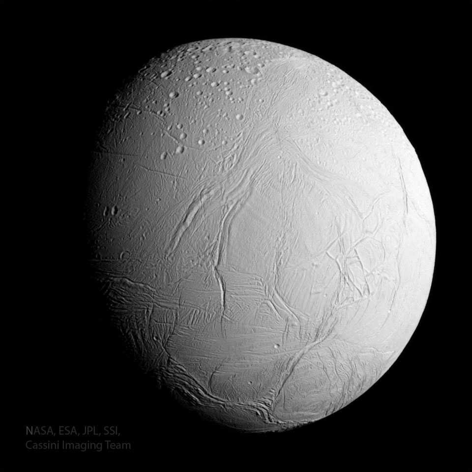 Der Saturnmond Enceladus im Bild ist in Echtfarben dargestellt. Er ist etwa zu drei Vierteln beleuchtet. Auf seiner hellen Oberfläche verlaufen tiefe Rillen. Oben sind kreisrunde Krater, die offenbar älter sind als der Rest seiner Oberfläche.