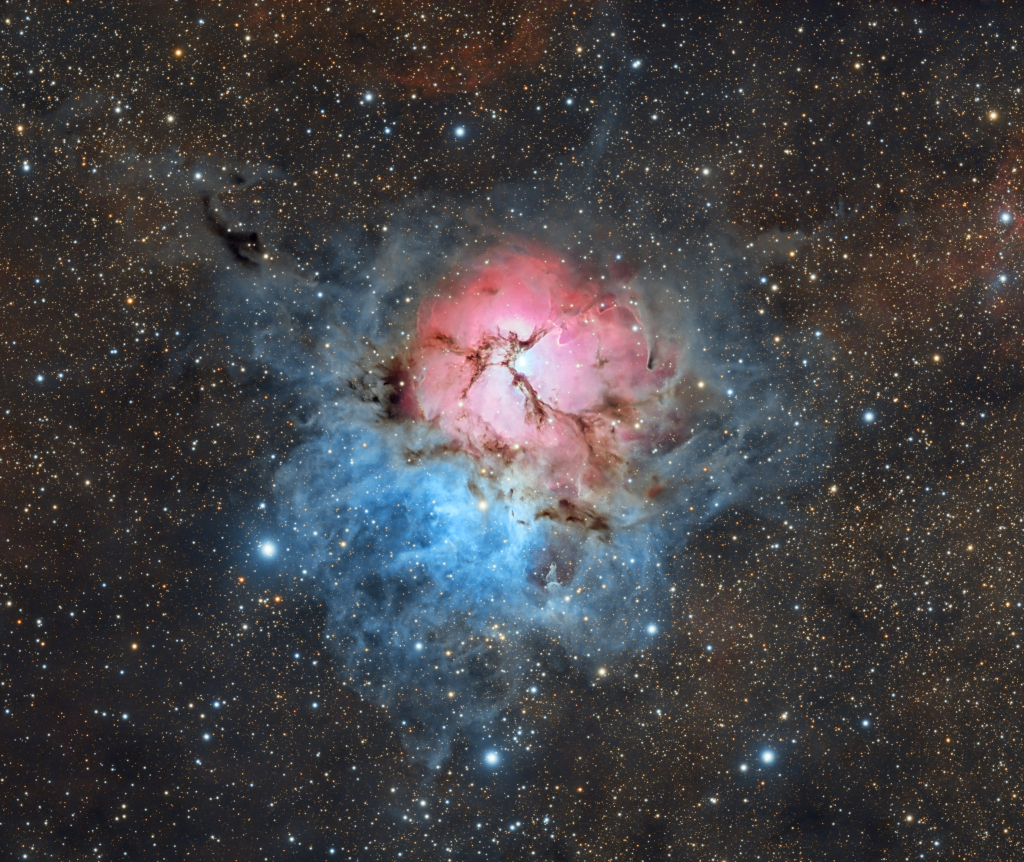 Der Trifidnebel M20 im Sternbild Schütze besteht aus drei Nebelarten. In der Mitte ist ein roter, runder Nebel mit hellen Sternen in der Mitte, der von dunklen Staubbahnen dreigeteilt wird. Außen herum verläuft unten ein blauer Reflexionsnebel. Das ganze Gebiet ist in einen Sternenteppich eingebettet.