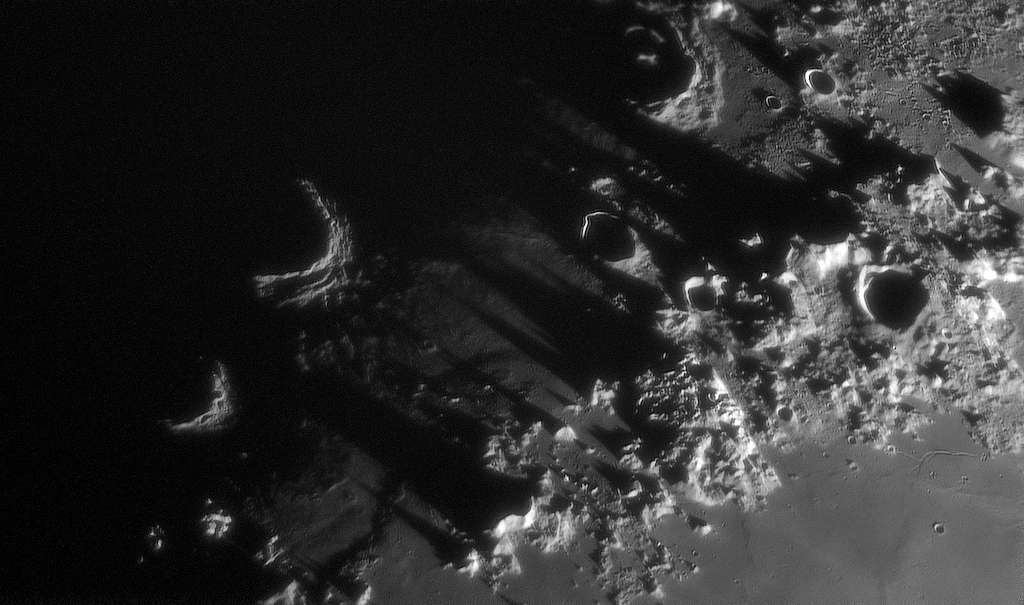 Die Nahaufnahme zeigt, wie in den Montes Caucasus die Sonne aufgeht. Die Schattengrenze läuft mitten durch das Mondgebirge. Links sind zwei Kraterwände gerade schon in der Sonne. Die Berge rechts werfen riesige, lange Schatten. Die Böden der Krater sind noch dunkel.