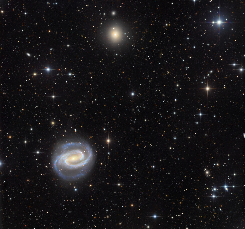 Links unten ist eine prachtvolle Spiralgalaxie mit markantem Zentralbalken und ausladenden Spiralarmen. Oben in der Mitte schimmert eine elliptische Galaxie.