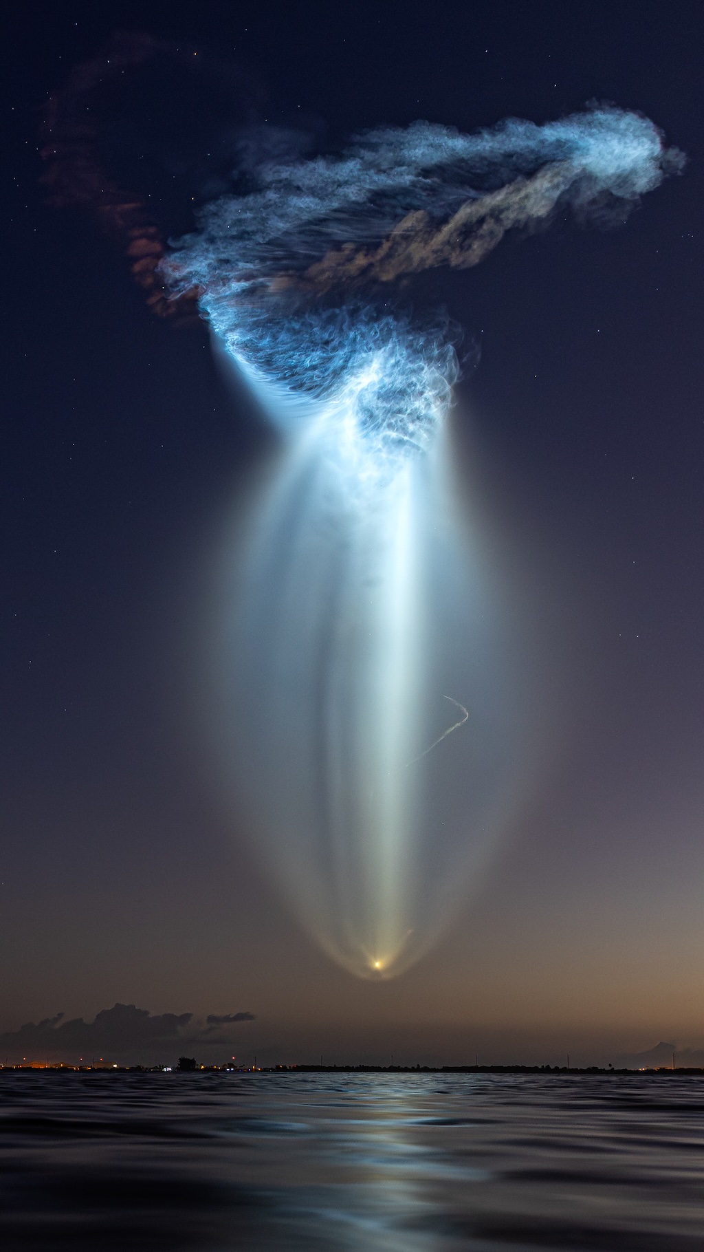 Über einem Gewässer schweben Abgasschwaden, die beim Start einer Falcon 9 entstanden. Sie wirken malerisch und fremdartig.
