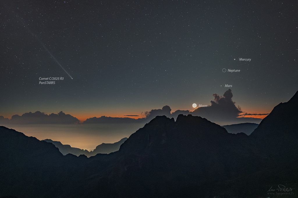 Links im Bild zeigt der Schweif des Kometen Komet C/2025 R3 PanSTARRS nach links oben. Rechts stehen die Planeten Mars, Neptun und Merkur und knapp über den Wolken der Mond. Das Bild entstand in den Bergen.
