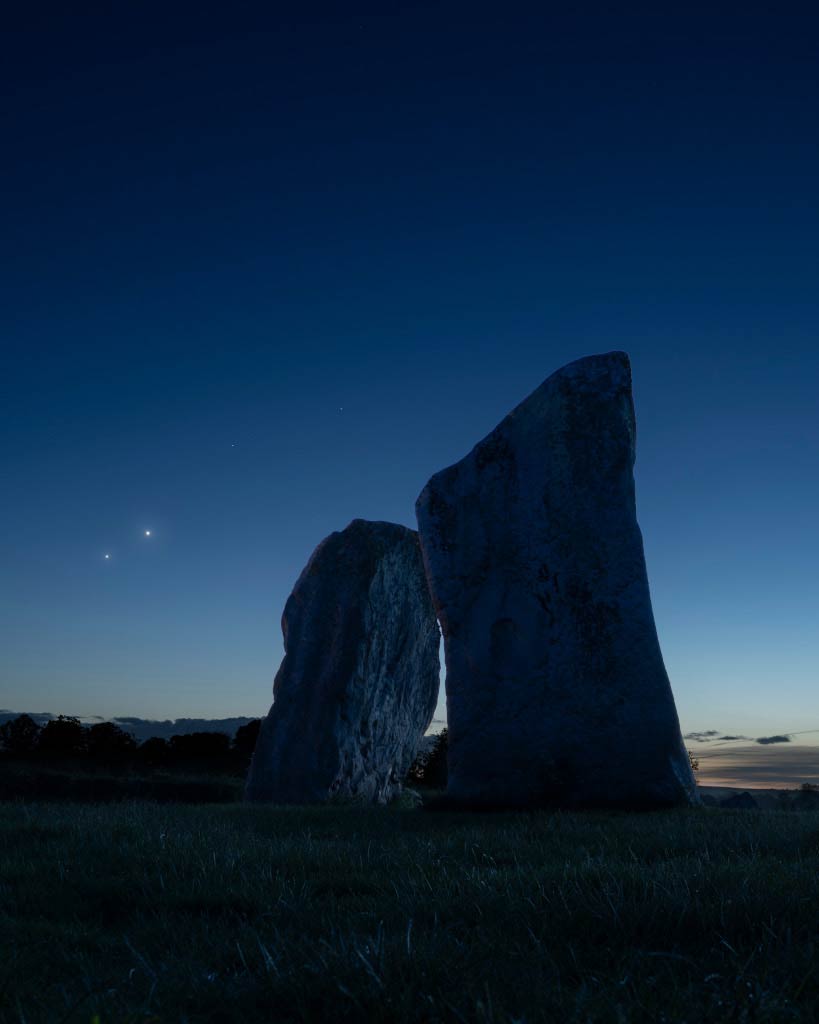 Am dämmerigen Abendhimmel leuchten zwei helle Lichter. Im Vordergrund ist eine dunkle Wiese, darauf stehen zwei riesige Steine, die leicht zueinander geneigt sind. Es sind die Megalithe "Adam" und "Eve" der Menhire in Avebury. Am Horizont sind Wolken und die Silhouetten von Bäumen. Direkt neben den Steinen stehen am Himmel zwei helle "Sterne", der hellere steht etwas rechts über dem anderen.