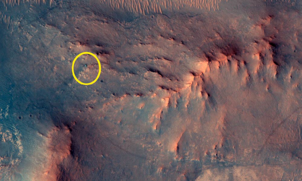 Die bergige, rötliche Oberfläche des Planeten Mars ist aus der Umlaufbahn abgebildet. Eine gelbe Ellipse markiert einen kleinen roten Punkt. Eine dunkle linienförmige Spur führt quer durch das Bild zu dem Punkt.