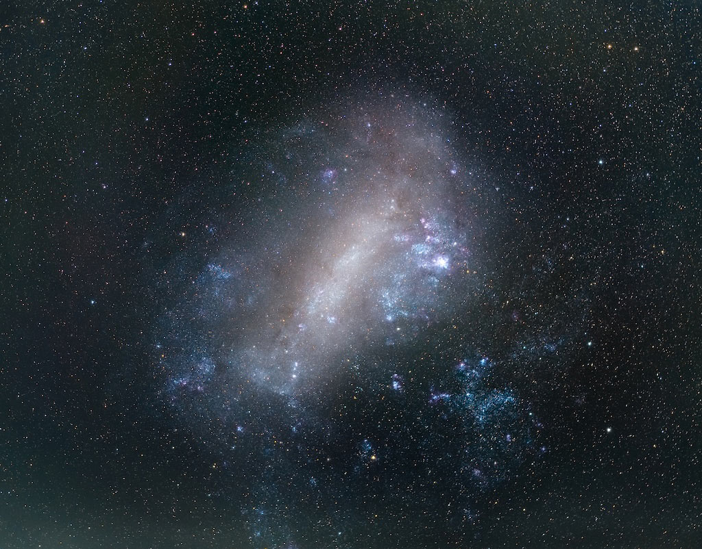Die Große Magellansche Wolke GMW füllt die Bildmitte. Sie ist von feinen, dicht verteilten Sternen umgeben. Die irreguläre Zwerggalaxie hat in der Mitte einen markanten Balken, der von einem diffusen Hof aus Sternen und Staub umgeben ist. Auch markante leuchtende Nebel sind in der Galaxie erkennbar.