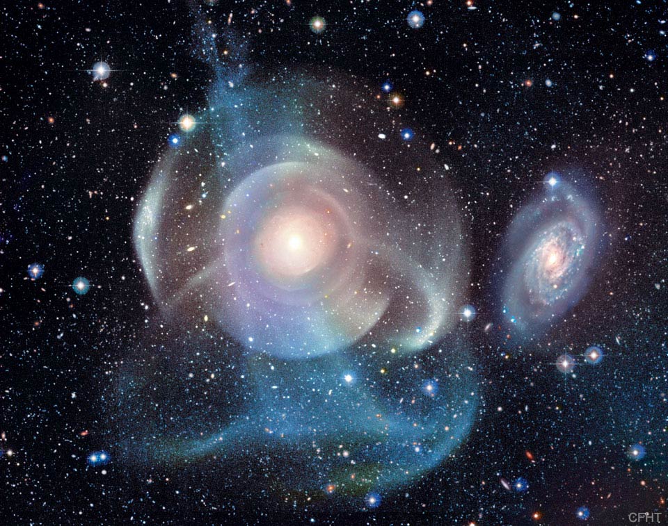 Die Galaxie mitten im Bild ist von schalenförmigen Hüllen umgeben. Sie wirkt kaum noch wie eine Spiralgalaxie. Daneben ist eine Spirale, die ebenfalls von Sternströmen umgeben ist.