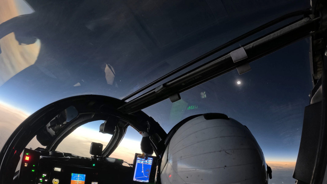 Der Blick aus dem Cockpit einer WB-57F zeigt die Sonne über dem Kopf des Piloten. Sie ist vom Neumond verdeckt, nur die Korona strahlt hell. Links neben der Bildmitte leuchtet die Venus, rechts Jupiter und Merkur. Der Himmel ist dunkel, doch der Horizont, der außerhalb des Mondschattens liegt, ist hell.